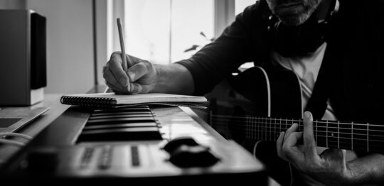 HeroImage Man sitting at keyboard guitar writing on notepad 540x262